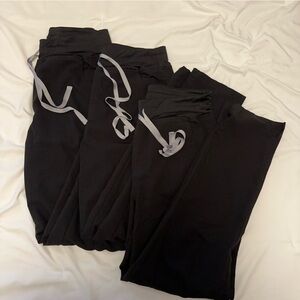 3 pairs of Figs High Waisted Yola Skinny Scrub pants in black.